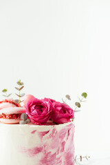 Beautiful birthday cake with pink cream cheese frosting decorated with macaroons and roses. Happy Valentine's day. Anniversary cake on the white background