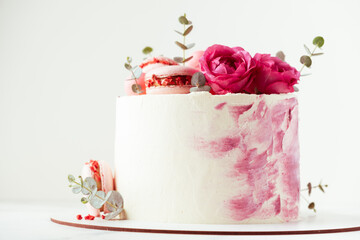 Beautiful birthday cake with pink cream cheese frosting decorated with macaroons and roses. Happy Valentine's day. Anniversary cake on the white background
