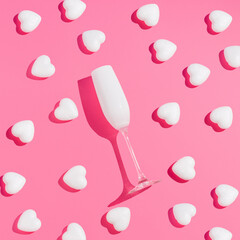 Creative love concept with white glass of champagne and hearts against light pink background. Minimal love or Valentine's Day idea. Flat lay.