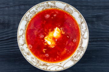 A plate of borscht (soup) with sour cream on a black table. Dinner.