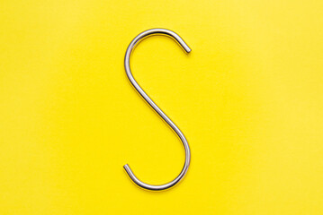 Bright Stainless Steel S hook isolated on a yellow background. Curved bent polished steel.