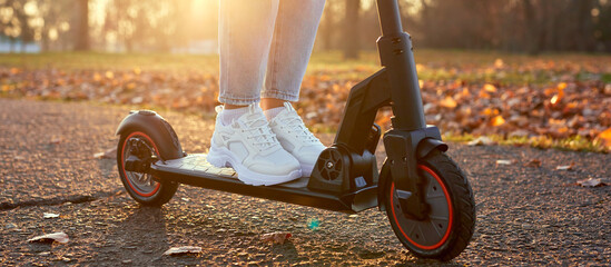 Woman discover city and park at sunset with electric scooter or e-scooter. Female Legs in sports...