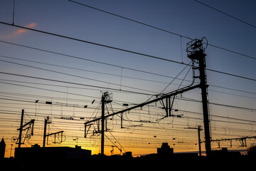 Silhouettes at sunset of electrical train equipment, wires, cables, lines and poles, Leuven, Belgium