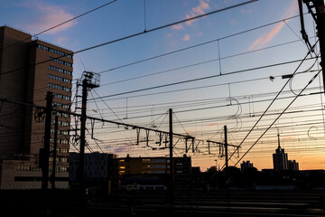 Silhouettes at sunset of electrical train equipment, wires, cables, lines and poles, Leuven, Belgium