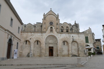 Fototapeta na wymiar St. John Baptist church in Matera, the facade made by white sandstone with the decorated entrance door, the arches, the statues and the bells.