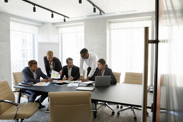 Multiethnic team of businesspeople analyzing startup project sales reports on meeting in boardroom....