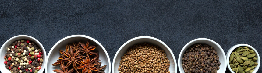 Frame banner with copy space of spices assorted multicolor peppercorns, cardamom, star anise, cumin, coriander, caraway in bowls on black background.