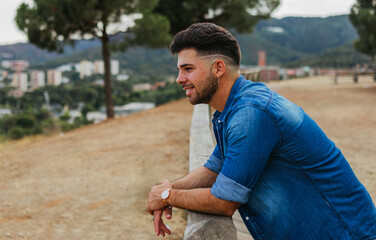 Side view waist up shot of a nice style guy leaning his arms on a railing observing something from a lookout point at the afternoon