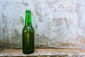 A bottle of beer stands against an old concrete wall