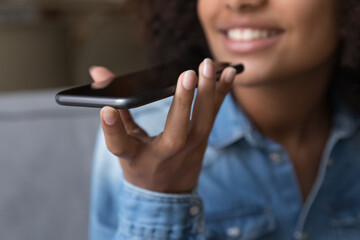 Happy teen African girl giving voice commands to virtual assistant on smartphone, speaking for...