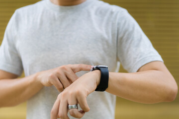 Fototapeta na wymiar Active Asian young sportsman using a smartwatch or smart fitness band to track his outdoor workout.