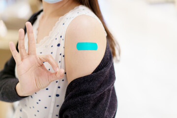 Happy Asian young woman wearing a protective face mask showing her vaccination spot on her arm.