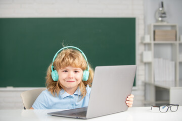 Cute smiling boy wearing headphones, study with laptop in classroom, listening audio lesson course. Elementary school and education.