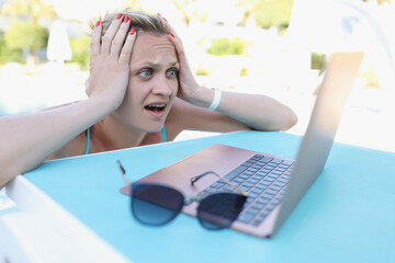 A young woman in the pool looks shocked into a laptop