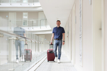 A happy man with a suitcase walks along the floor of the hotel