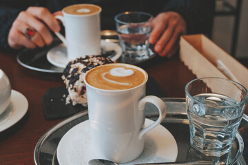 Fragrant cappuccino with a beautiful foam in a white mug on the table. Coffee for two. Hands holding a cup of coffee with almond milk
