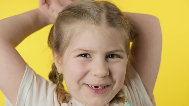 Happy girl with toothless smile looking at camera at yellow background. Loss of deciduous tooth. Cheerful child with pigtails expressing positive emotions. 4K, UHD