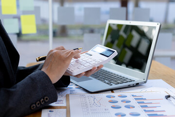 Businessman using a calculator to calculate numbers on a company's financial documents, he is...