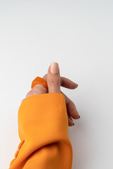 Close shot of a thin graceful hand of a girl with a nude pastel spring trendy manicure and a big ring on her finger in an orange jacket on a white background