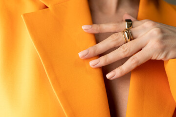 Close shot of a thin graceful hand of a girl with a nude spring trendy manicure and a gold ring on her fingers in an orange jacket