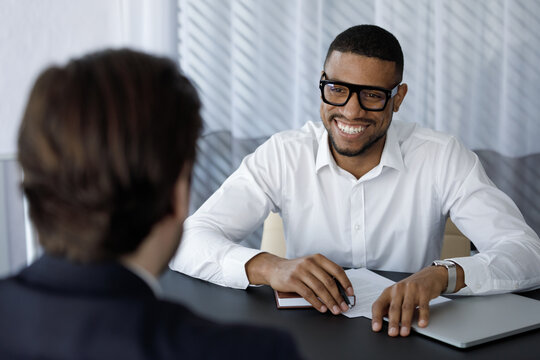 Happy African intern meeting with mentor, company coach, listening to teacher, smiling, laugh. Job seeker meeting business owner for interview. Manager, banker giving consultation to client