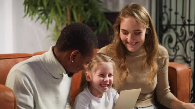 Girl laughs looking at old picture with mother and father