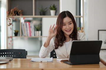 Portrait of smiling asian woman waving hello talking on video call. Successful young woman sitting...