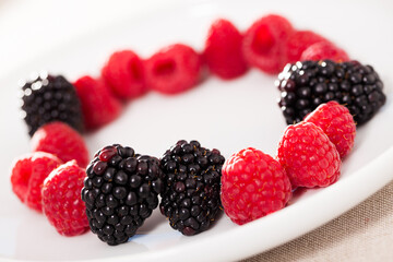 raspberries and blackberries laid out on a white plate in circle