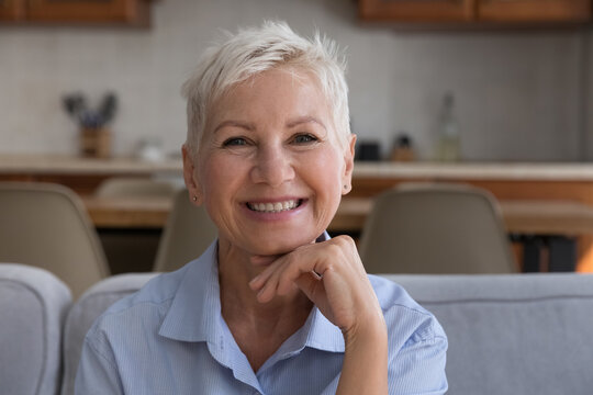 Happy stylish senior 60s woman home head shot portrait. Cheerful blonde short haired middle aged lady in casual looking at camera with toothy smile, posing, laughing. Video call screen