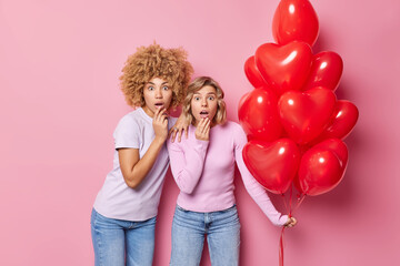 Omg Valentines day is coming. Shocked two women stare impressed prepare for party hold bunch of red heart shaped balloons isolated over pink background. Festive event and celebration concept