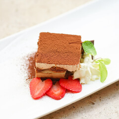 Tiramisu. A tiramisu cake served with slice of strawberries, whipping cream and mint leaf.