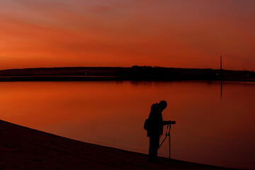 A silhouette of a photographer at sunset. A man shooting a landscape in the evening with a tripod © V_Saratovtseva