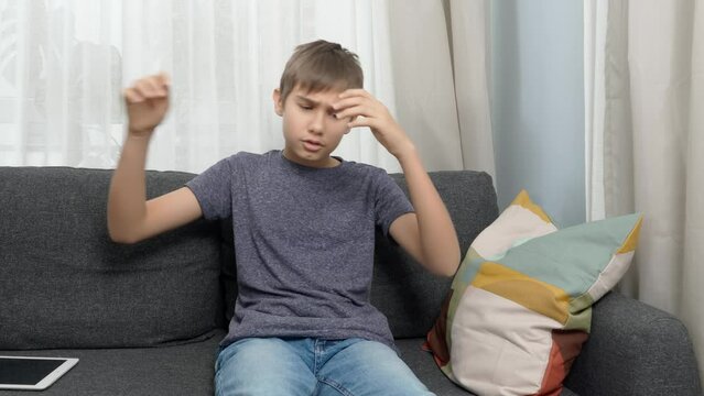 Teenage boy reads bad news on digital tablet. Sad unhappy kid feeling annoyed and throwing his tablet on the sofa. Learning difficulties, sadness, desperation, emotional problems, exam or test failure
