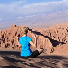 Woman doing spiritual yoga on sand dune in windy Atacama desert mountain landscape with impressive view flying hair
