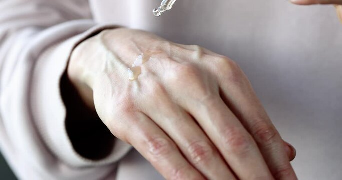 Female hand drips essential oil on skin of hand for moisturizing closeup