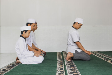 Side view of a group of Muslims praying in congregation with hand gestures pointing at tahiyat at...
