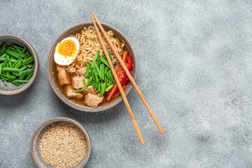 Ramen noodle soup with chicken, vegetables and eggs. Gray rustic concrete background. Top view. Japanese food. - obrazy, fototapety, plakaty