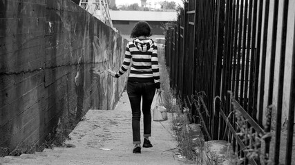 A woman in a striped sweatshirt walks along the sidewalk along a metal fence.