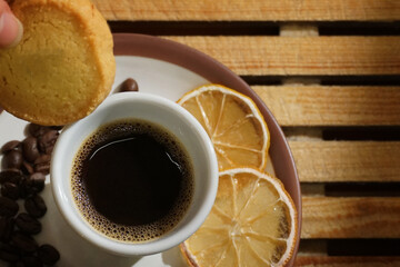 Colazione con tazzina di caffè e biscotto, chicchi di caffè su fondo di legno