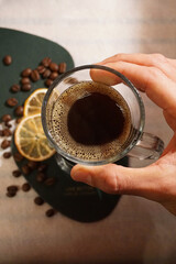 Caffè in tazza trasparente con mano, arance, chicchi di caffè e relax