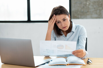 Stressed caucasian business woman sitting at the desk in the office analyzes a bad sales chart. Female has financial problems, lack of finances, bankruptcy concept