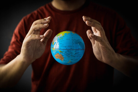 A globe floats between hands on a man's chest. Earth day concept with low key tone photo