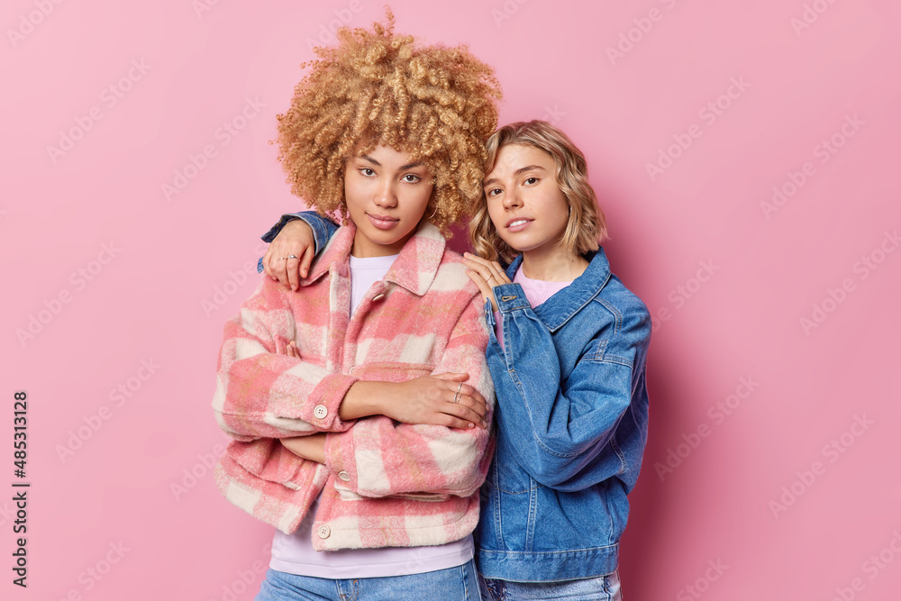 Wall mural beautiful young women embrace and look directly at camera wear fashionable clothes pose for making m