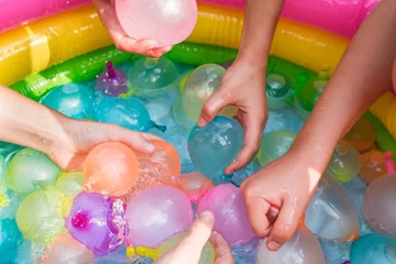 Poster Water balloon games for kids. Close up of girls filling up water balloons at sunny day. Summer fun outdoor activities for children concept © tgordievskaya