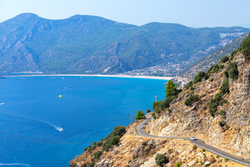 Obraz premium Curvy turn of mountain highway with blue sky and sea on a background. Fethiye Oludeniz beach view from the hill. Oludeniz beach is one of the most beautiful beaches in Turkey.