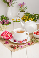 Herbal tea with rosehip, chamomile and meadowsweet in a white cup on a white wooden table with flowers