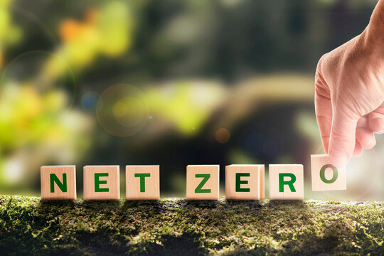 Net zero 2050 Carbon neutral. Net zero greenhouse gas emissions target. Climate neutral long strategy. No toxic gases. Hand puts wooden cubes with netzero icon in green background copy space.