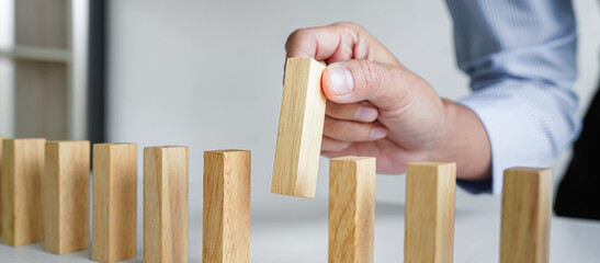 Risk and strategy in business, Close up of business woman hand gambling placing wooden block on a line of domino - obrazy, fototapety, plakaty
