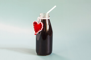 Transparent bottle with grape juice and a red heart on the neck light background.