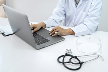 A female doctor is typing about symptom and treatment method of patients on laptop while working to diagnose